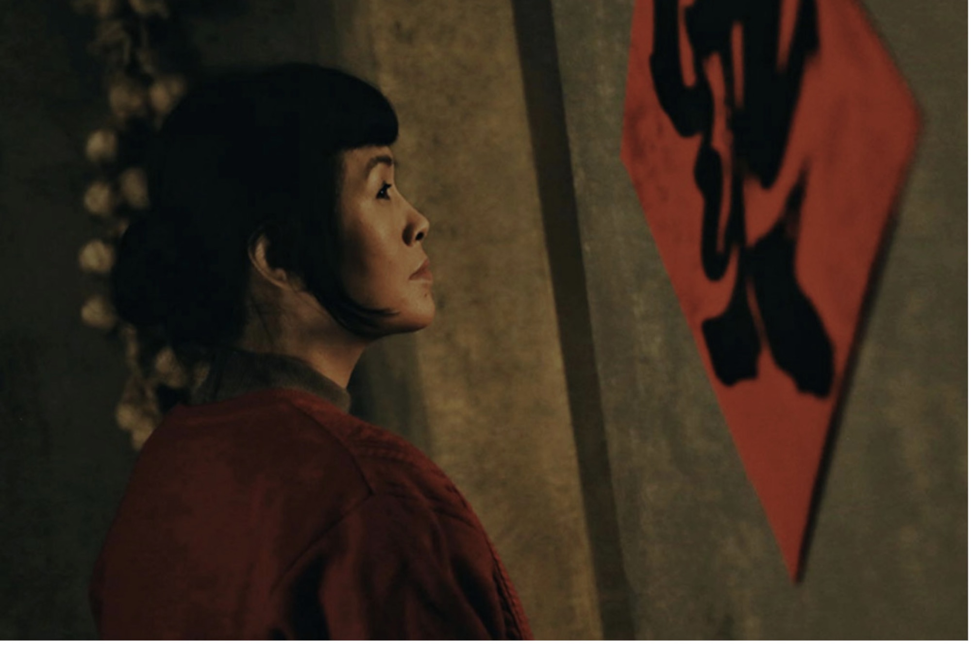 Film still of Grace Chang in a red costume looking up at a calligraphy banner