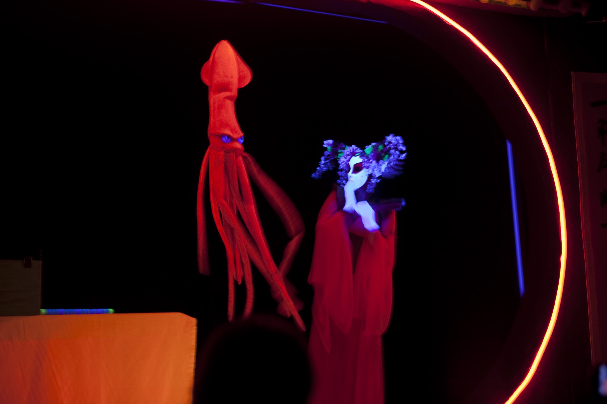 Blacklight puppet theater scene from Magical Ocean with a glowing red squid puppet and masked performer